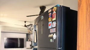 A modern kitchen with a black refrigerator, wooden flooring, and a ceiling fan. - The Nest Noida (Noida)