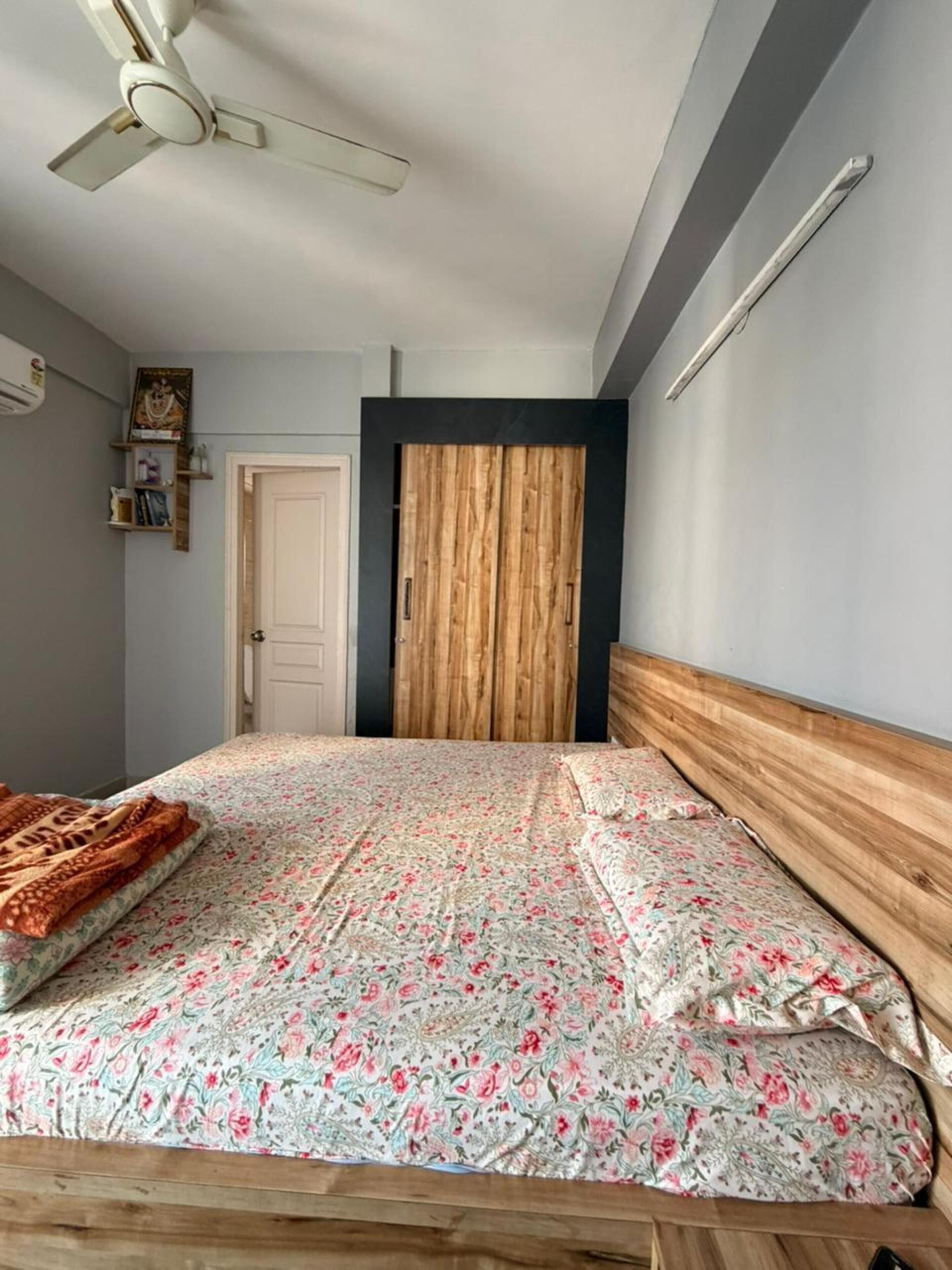 A bedroom with a bed, a ceiling fan, a wardrobe, and a door.