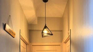 A hallway with a closed door, a hanging light fixture, and a small sign on the wall. - The Nest Noida (Noida)