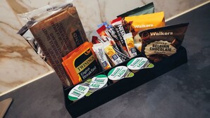 Ett bricka med olika förpackade snacks, inklusive Twinings English Breakfast-te, Walkers-chips och belgiska chokladkakor.