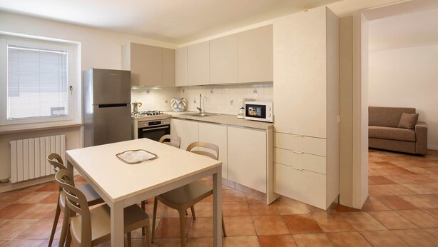 A compact kitchen with a dining table, chairs, a refrigerator, a stove, and a microwave. - Casa Gloria - in the center of San Zeno di Montagna (San Zeno di Montagna)