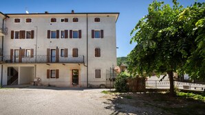 A multi-story building with a balcony, a gravel driveway, and a tree. - Casa Gloria - in the center of San Zeno di Montagna (San Zeno di Montagna)