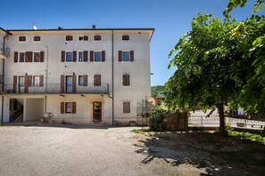 A multi-story building with a balcony, a gravel driveway, and a tree. - Casa Gloria - in the center of San Zeno di Montagna (San Zeno di Montagna)