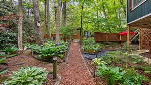 Un jardin avec un sentier, des structures en bois et un bâtiment surmonté d’un parasol rouge.