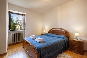 Ein Schlafzimmer mit Bett, Fenster, Heizkörper und Nachttisch mit Lampe.