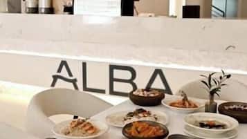 A dining area with a table set for a meal, a reception desk, and a sign with the word 'ALBA'.