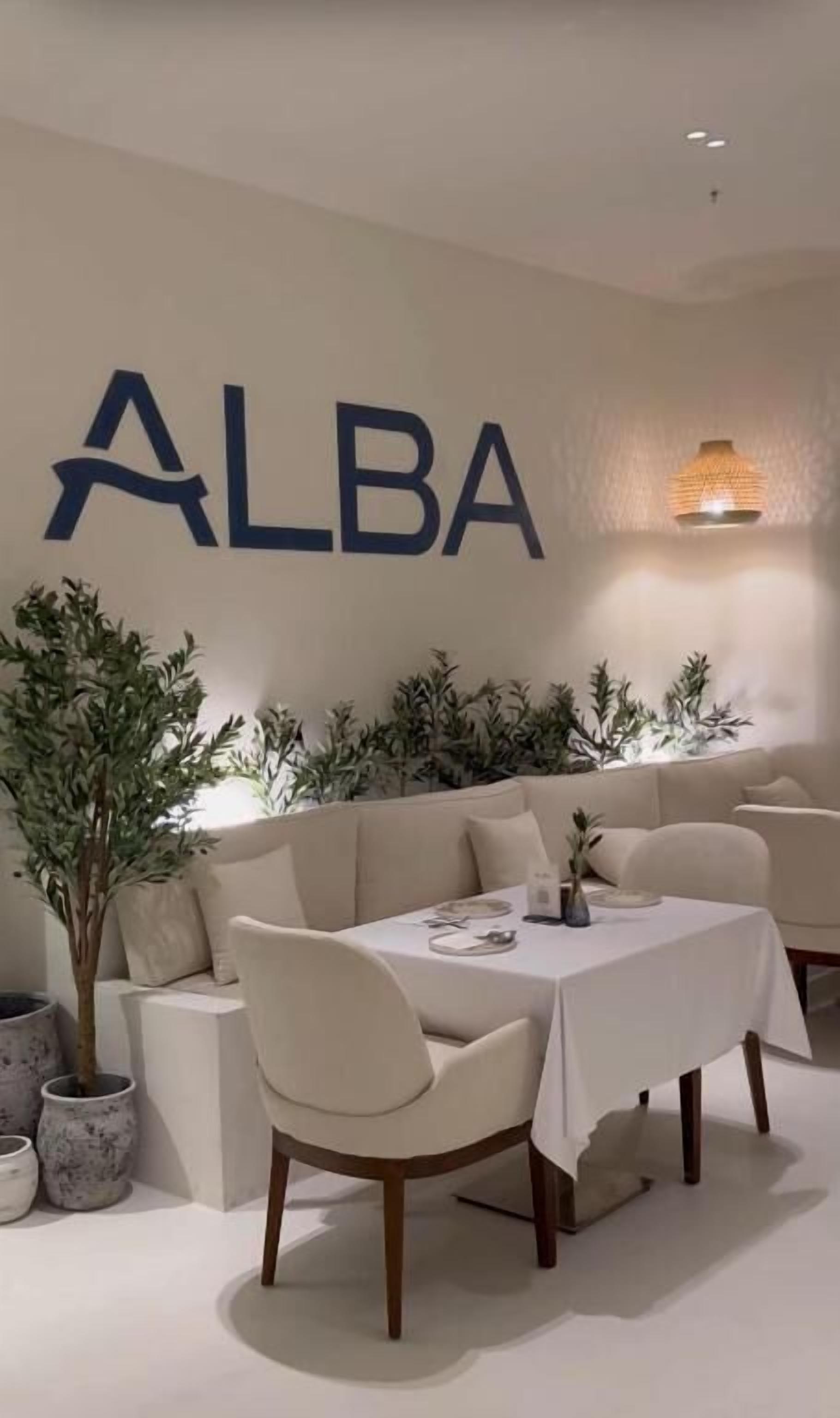 A modern interior with a sofa, a dining table with chairs, and a wall-mounted sign reading 'ALBA'.