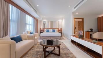 A hotel room with a bed, a sofa, a coffee table, a TV, and a bathroom visible through an open door.
