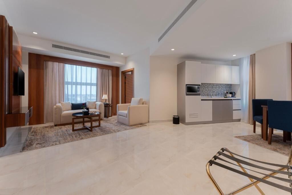 A modern living room with a sofa, coffee table, and a TV. There is a kitchen area with cabinets and a microwave.