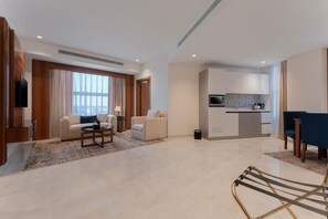 A modern living room with a sofa, coffee table, and a TV. There is a kitchen area with cabinets and a microwave. - Corp Yanbu Hotel B1 (Yanbu)