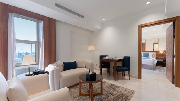 A hotel room with a sofa, a dining table, and a bed. - Corp Yanbu Hotel B1 (Yanbu)