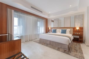 Una habitación de hotel moderna con una cama grande, un escritorio y un ventanal con cortinas.