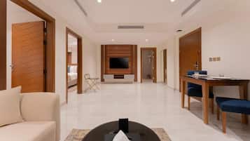 A hotel room with a sofa, a dining table with chairs, a TV mounted on the wall, and a small table with a tissue box.