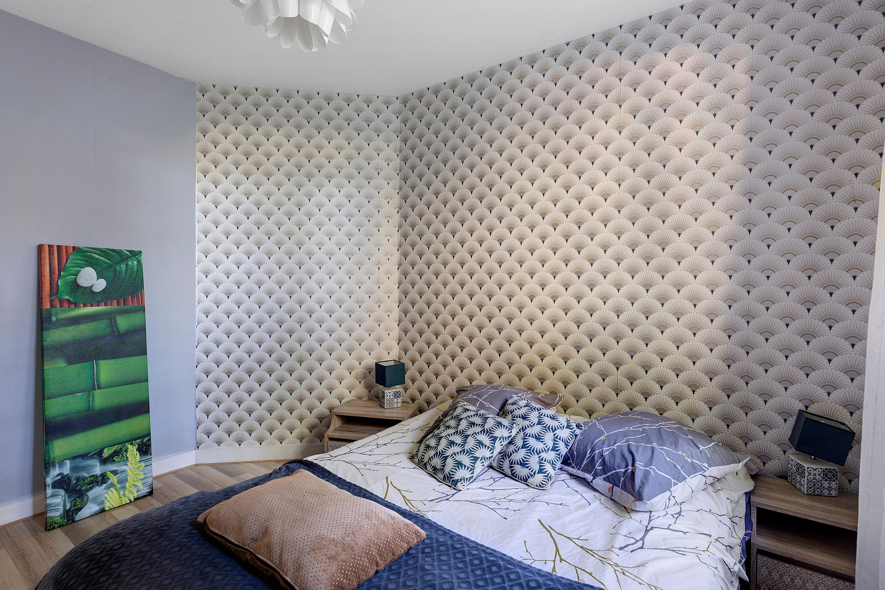 Une chambre à coucher avec un lit, des oreillers, une table de chevet, un tableau et un papier peint à motifs.