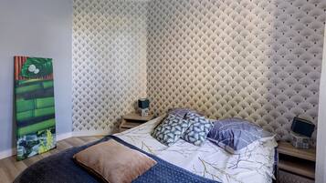 Une chambre à coucher avec un lit, des oreillers, une table de chevet, un tableau et un papier peint à motifs.