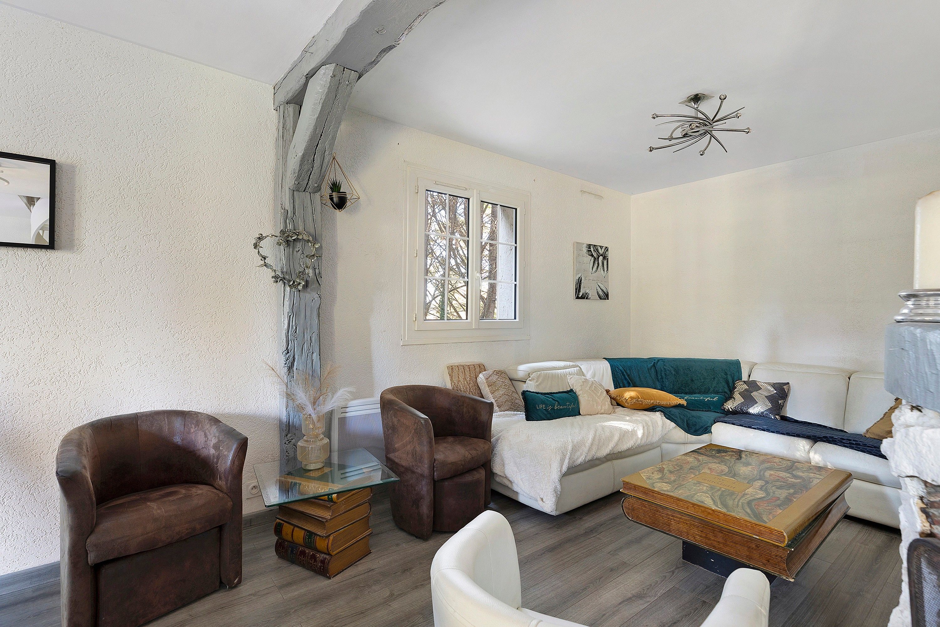 Ein Wohnzimmer mit einem weißen Sofa, zwei braunen Sesseln, einem Glastisch mit Büchern und einem dekorativen Metallteil an der Decke.