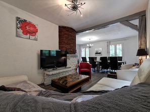 Ein modernes Wohnzimmer mit Flachbildfernseher, Kamin, Essbereich und Blick durch eine offene Tür.