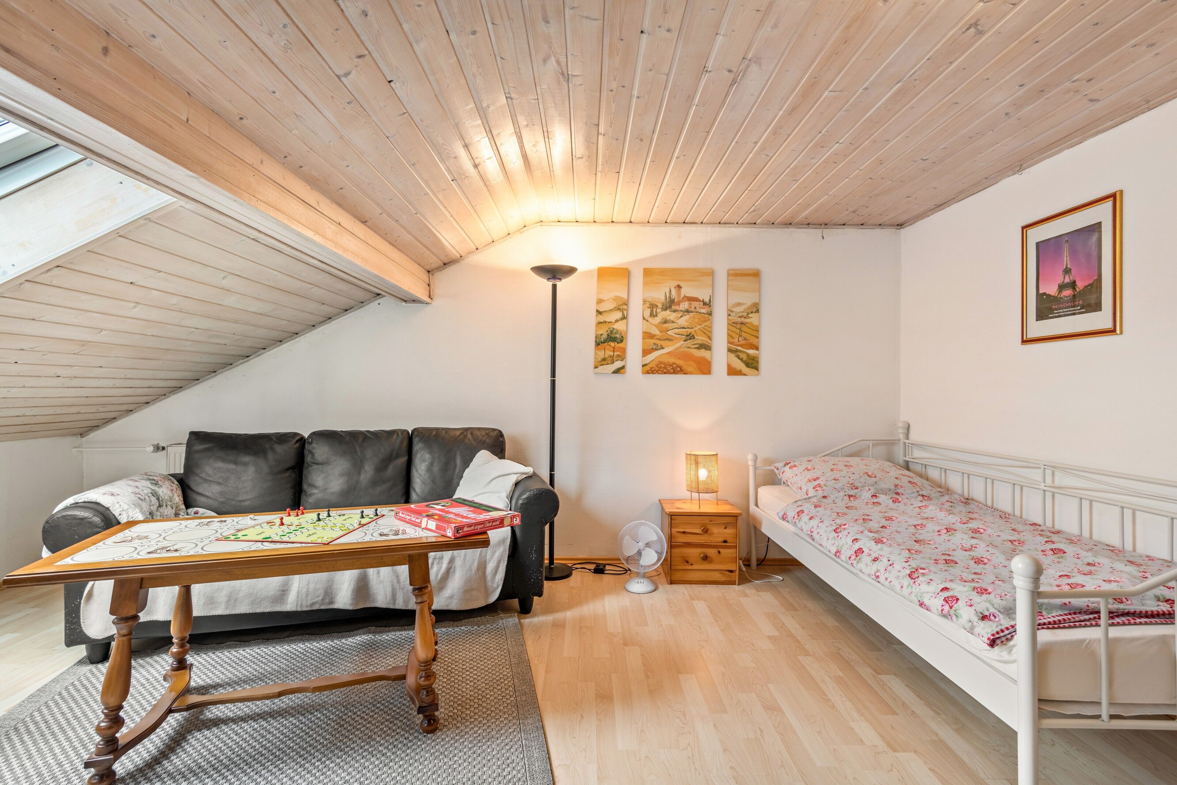 Een kamer met een stapelbed, een slaapbank, een tafel met een spel, een lamp en een foto van de Eiffeltoren.