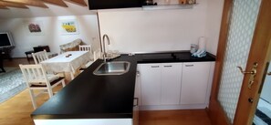 A compact kitchen with a black countertop, white cabinets, a stainless steel sink, and a dining area with a table and chairs.