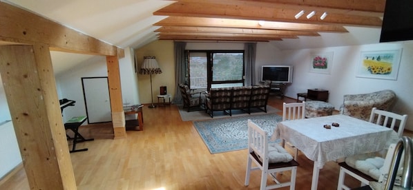 A cozy living room with a wooden ceiling, a TV, a sofa, and a dining table with chairs.
