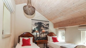 A bedroom with two wooden beds, a hanging light fixture, a painting on the wall, and a window. - The Coach House Cottage (Dromineer)