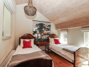 A bedroom with two wooden beds, a hanging light fixture, a painting on the wall, and a window. - The Coach House Cottage (Dromineer)