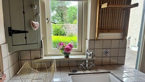 A kitchen with a window, a sink, and a vase with flowers. - The Coach House Cottage (Dromineer)