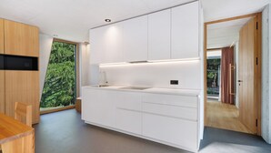 Une cuisine moderne avec des meubles blancs, un évier encastré et une grande fenêtre donnant sur la forêt.