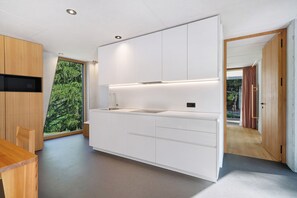 Cozinha moderna com armários brancos, pia embutida e uma grande janela com vista para a floresta.