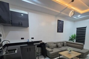 Ein modernes Wohnzimmer mit einer Couch, einem Couchtisch, einer Küchenzeile mit Spüle und einer Deckenleuchte.