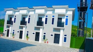 A modern building with a symmetrical facade, multiple balconies, and a paved courtyard. - Devon's Stylish 1BR Apartment + Pool, Apo Resettlement Abuja (Abuja)
