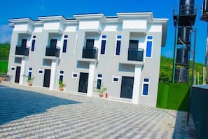 Ein modernes Gebäude mit einer symmetrischen Fassade, mehreren Balkonen und einem gepflasterten Innenhof.