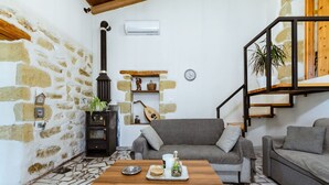 A cozy living room with a stone wall, a fireplace, a sofa, a coffee table, and a staircase. - Xanthippi s Traditional House in Pemonia (Apokoronas)