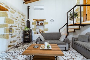 A cozy living room with a stone wall, a fireplace, a sofa, a coffee table, and a staircase. - Xanthippi s Traditional House in Pemonia (Apokoronas)