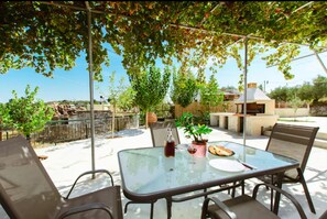 An outdoor patio with a glass table, chairs, a potted plant, and a grill. - Xanthippi s Traditional House in Pemonia (Apokoronas)