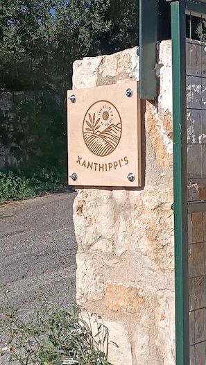 A wooden sign with a sun and landscape design, mounted on a stone wall. - Xanthippi s Traditional House in Pemonia (Apokoronas)
