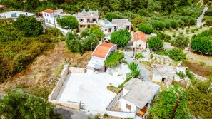 An aerial view of a residential area with houses, some with red roofs, surrounded by greenery and a small road. - Xanthippi s Traditional House in Pemonia (Apokoronas)
