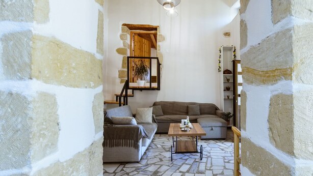 A cozy living room with a stone floor, a wooden staircase, and a bookshelf. - Xanthippi s Traditional House in Pemonia (Apokoronas)