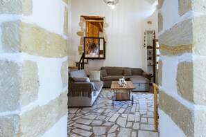 A cozy living room with a stone floor, a wooden staircase, and a bookshelf. - Xanthippi s Traditional House in Pemonia (Apokoronas)