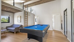 A modern room with a pool table, a grey sofa, a small round table, and a window with a view of trees. - VillaVilla 975 - Hasmark Strand, Fyn og øer (Otterup)