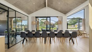 A modern dining area with a long table, chairs, and large windows offering a view of the outdoors. - VillaVilla 975 - Hasmark Strand, Fyn og øer (Otterup)