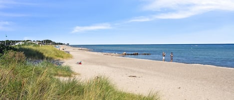 En sandstrand med klar himmel, några få personer och ett lugnt hav.