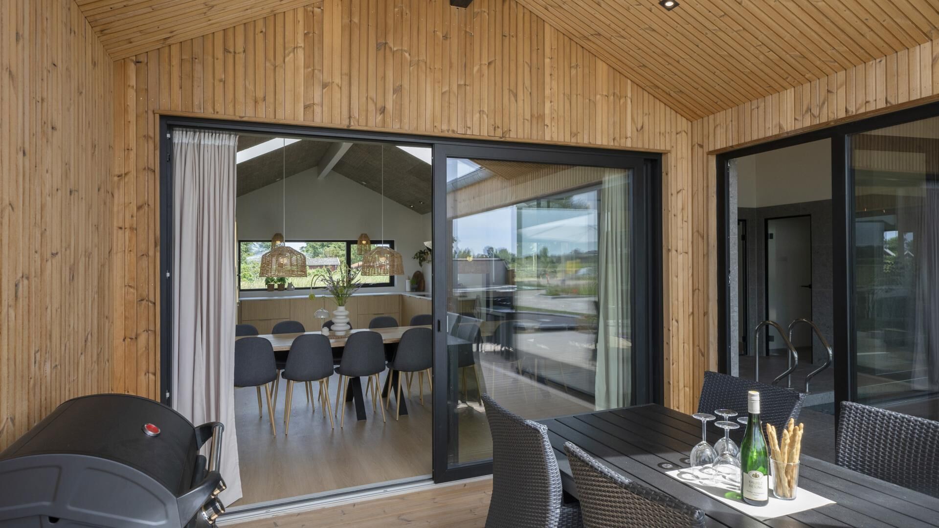Ein moderner Essbereich mit Glastür zum Patio, ein gedeckter Tisch mit Gläsern und einer Flasche sowie ein Grill draußen.