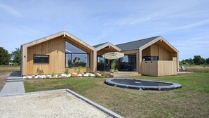 Une maison moderne en bois, dotée de grandes fenêtres, d’un patio couvert et d’un trampoline.