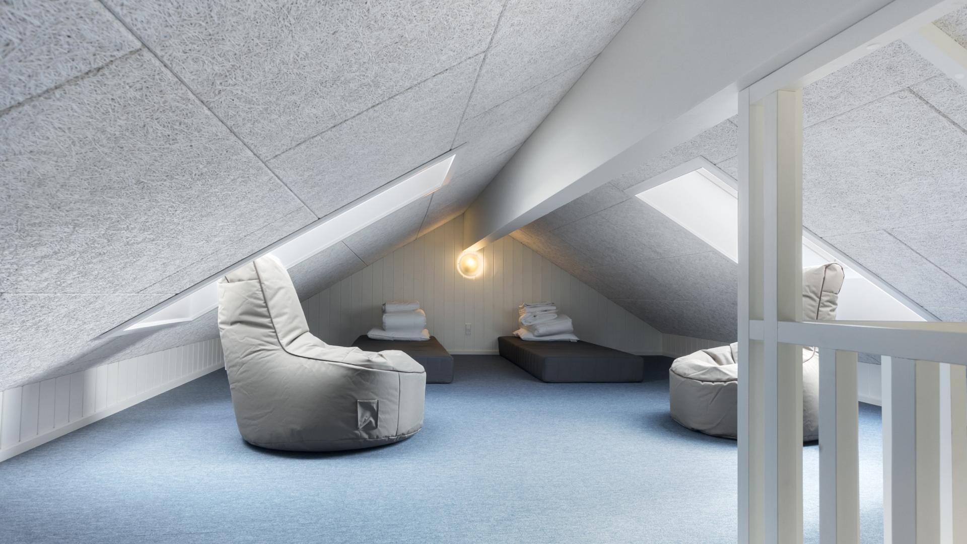 A modern attic room with a sloped ceiling, a built-in bench, and a wall-mounted light fixture.