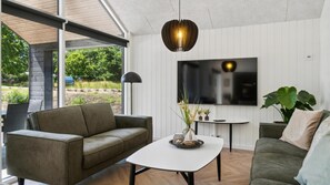 Ein modernes Wohnzimmer mit einer Couch, einem Couchtisch, einem Fernseher und einer Pendelleuchte.