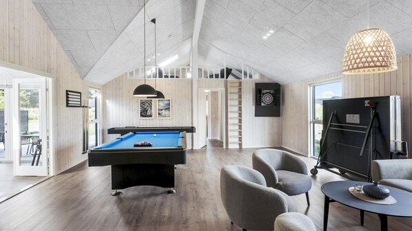 Un espacio interior moderno con mesa de billar, asientos cómodos y un ventanal amplio.