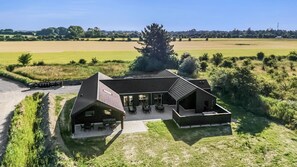 A modern house with a large patio area, surrounded by open fields and a prominent tree. - VillaVilla 948 - Marielyst, Lolland/Falster/møn (Idestrup)