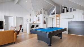 Ein modernes Wohnzimmer mit Billardtisch, braunem Sessel und Fernseher.