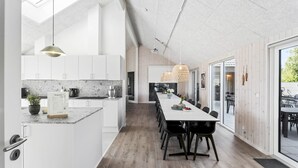 Moderni keittiö, jossa on valkoiset kaapit, marmorinen työtaso sekä ruokailutila, jossa on pitkä pöytä ja tuolit.